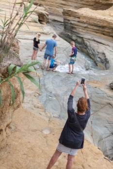 Woman taking candid photo. Parents holding hands while watching the son enjoying the water flowing from the cliff. Family bonding moments and travel get away