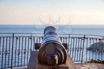 A cannon pointing towards the sea. The ancient artillery sitting above the concrete block. A calm sea surrounds the statue. Revolutionary war machinery