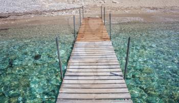 Patterned dock over the water. Wooden post supporting the walk bridge.Crystal clear water glittering under the sun. Scenic view of a travel destination