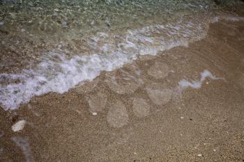 Wavy foamy crystal clear ocean water washing up on sandy beach shore. White waves on sand. Relaxation. Summer vacations. Leisure. Traveling abroad in Corfu Greece