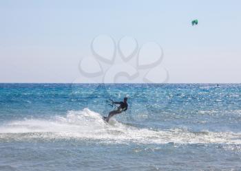 A man in full gear suit above the ocean. The athlete holding firm the handle while gliding in the sea. Ski boarding in action. Water sports ideas and beach activities