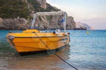 A yellow private boat in the beach. The speed water vehicle docking in the shoreline. A mountainous rock formation secluding the area. Mode of transportation in island hopping