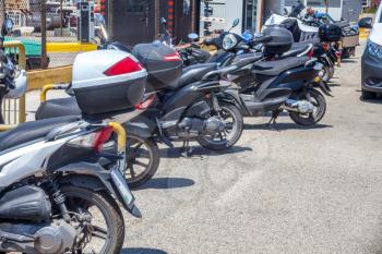 Paleokastritsa, Cofru, Greece- MAY 10, 2018 Motorcycles piling up along the roadside during bright sunny day. The two wheel vehicles parks beside the metal fence. Car passing by