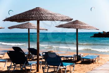 Lounge Chairs under Straw Umbrellas on beautiful sandy beach in Corfu Greece. Seashore great view. Transparent turquoise water. Summer vacation time. Relaxation in chair and umbrella