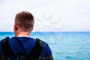 Head of the man with blue sea in the background. Blurred sea in the background. Emotional concept with man looking at the sea. Adventure concept with man and the backpack.