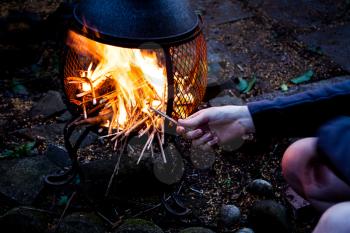 Man sitting by the open fire and firing with wood twigs. Camping fire in the twilight night. Wooden camp fire in the night. Preparing barbecue fire in the outside
