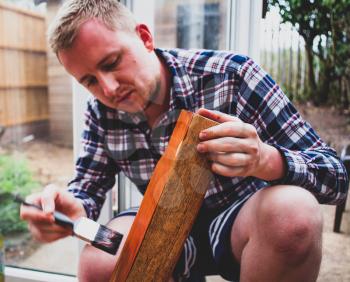Young man painting wooden board with brush. Working man with paintbrush in the hand, coloring wooden furnitures. Home improvement concept with renovating furniture