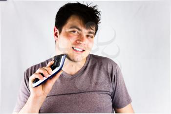 A young man shaving his chin with an electric shaver. Teenager holding his electric trimmer. Handsome young man is using an electric razor  and looking at camera