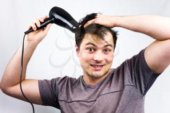 Young man smiling while he dries his hair. Teenager holding hair electric fan. Young man dries hair with an electric fan. Preparing a hair for going to a night life.