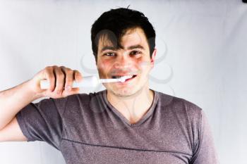 Close-up of young man brushing teeth with electric toothbrush. Joyful young man smiling during morning teeth brushing. Health and beauty concept image with brushing teeth