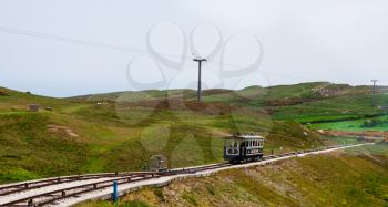 View from the top of the Great Orme Mountain in LLandudno, Wales. An industrial vintage funicular on a steep slope going down the railway in a green park