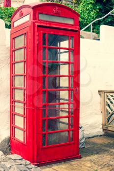 An old classic British red phone booth. Traditional red phone box on street. Not working vintage style image of typical red telephone booth with broken window glasses