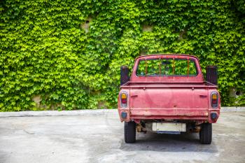 LLandudno, Wales, UK - MAY 27, 2018 Vintage pickup truck seen on the garage. The traditional vehicle park in front of the concrete wall growing with shrubs. Spare tire hanging below the trunk. Old, non urban mode of transportation