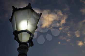 An incandescent bulb properly covered with glass glowing in antique street lamp post.The medieval european lamp post is made of cast steel is made of an ornate top.