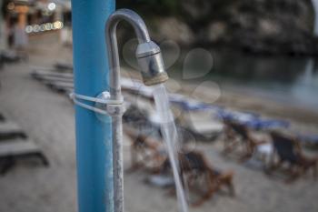 Water flowing through a tap and it is clamped as well as trapped in a beach resort. There it is evening with lights switched on in the shops with sunbath chairs arranged neatly.