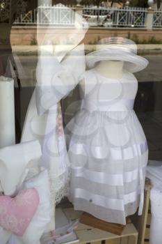 Nice baby girl white dress and ribbon displayed from a shop. Wardrobe is top with a hat and striped with a silk. It is exhibited or parade in the botique for the customer to see. 