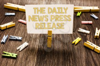 Text sign showing The Daily News Press Release. Conceptual photo announcing big news or speak to people Clothespin holding white paper note several clothespins wooden floor