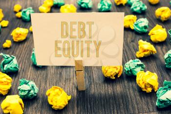 Handwriting text writing Debt Equity. Concept meaning dividing companys total liabilities by its stockholders Clothespin holding light pink note paper crumpled papers several tries