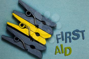Conceptual hand writing showing First Aid. Business photo text Practise of healing small cuts that no need for medical training Gray yellow vintage clothespins clear background Holding things