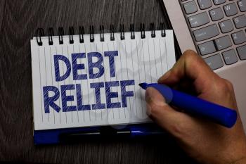Writing note showing Debt Relief. Business photo showcasing partial or total remission of it especially those by countries Man holding marker spiral notebook computer keyboard wooden background