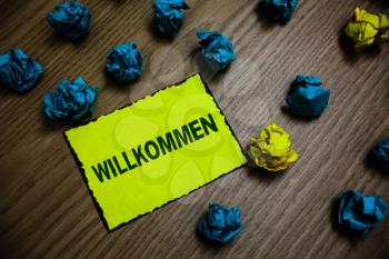 Word writing text Willkommen. Business concept for welcoming people event or your home something to that effect Yellow piece paper reminder lots crumpled papers several tries wooden floor