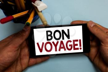 Conceptual hand writing showing Bon Voyage. Business photo showcasing used express good wishes to someone about set off on journey Man holding cell phone looking messages apps cup markers