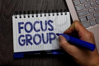 Writing note showing Focus Group. Business photo showcasing people assembled to participate in discussion about something Man holding marker spiral notebook computer keyboard wooden background