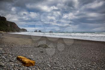 Stormy weather approaching an orange rock on a beach in New Zealand