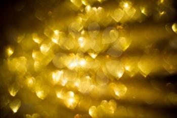 Festive background with defocused golden glitters, bokeh in a shape of a heart.