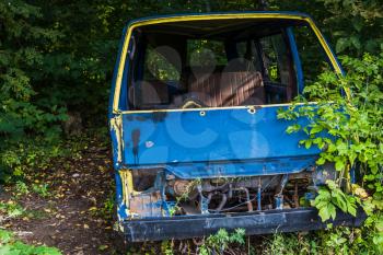 Abandoned big broken car on blue color in the woods.