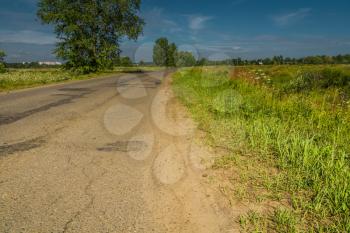 Old cracked, damaged asphalt road in countryside at sunny day.