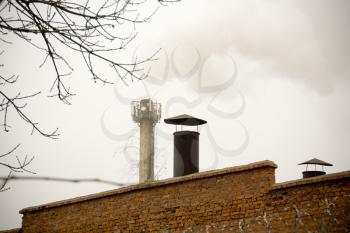 Old factory stack with dense smoke over grey sky.