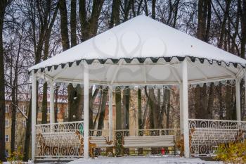 Decorative wooden alcove with benches in the city park at the winter time.
