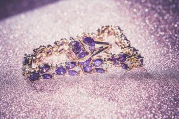 Decorative golden bracelet with purple amethysts on glittering background.