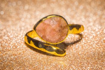 Fashion yellow gold ring with an orange sunstone on glitter background.