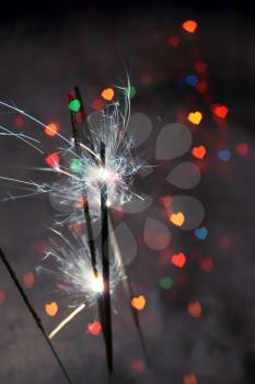 Bengal fire, sparkler and colorful bokeh in a shape of a heart, holiday background.