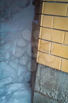 Big snowdrift near brick wall of rural house.