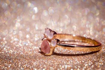Fashion gold ring with natural pink quartz in animal paw shape on glitter background.