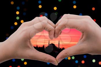 Islamic mosque view seen behind a heart shaped hand