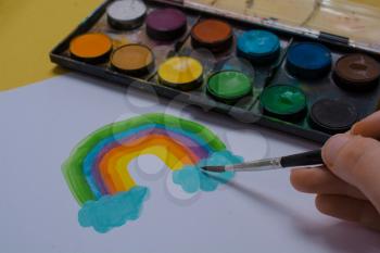 Kids hand painting rainbow with brush during coronavirus quarantine at home.