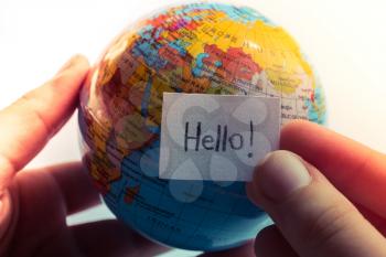 Hand holding notepaper with HELLO wording on model globe