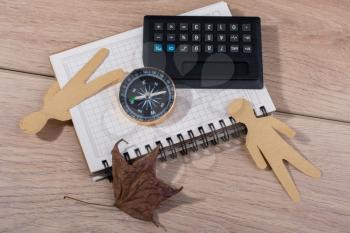 Paper men, compass and calculator on notebbok