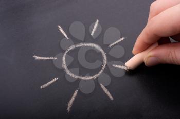 Hand drawing sun by chalk with light ray shape on blackboard background