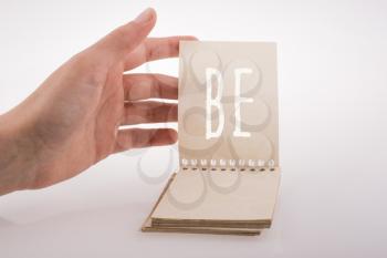 Hand holding notebook with be word on a white background
