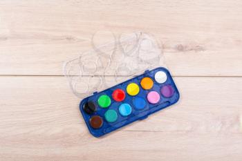 Watercolor paint box on a sheet of paper a wooden background