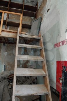 Steep wooden staircase crumbling attic and fire extinguisher sign in abandoned factory interior.