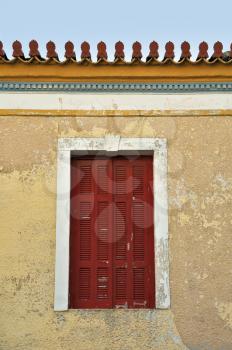 Red window shutter and weathered wall of a neoclassical building in Athens, Greece.