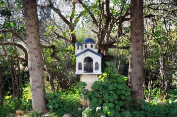Small street church shrine surrounded by trees and plants. Athens, Greece.