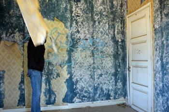 Obscured figure in abandoned house. Empty room with weathered torn wallpaper.