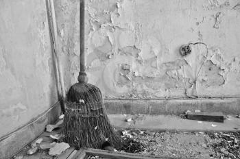 Dusty straw broom on filthy floor of abandoned house. Black and white.